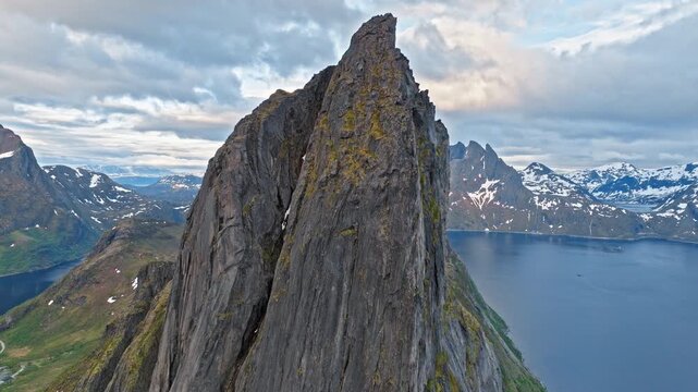 Drone aerial revealing the sharp pinnacle of Segla mountain above the Norwegian fjord on Senja Island. Iconic Arctic peak surrounded by dramatic coastal mountains.