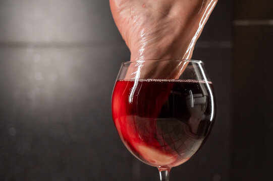 Foot fetish. A woman dips her toes in a glass of red wine.