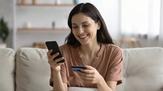 Young adult woman smiling while shopping online using smartphone and credit card showing digital consumer lifestyle at home