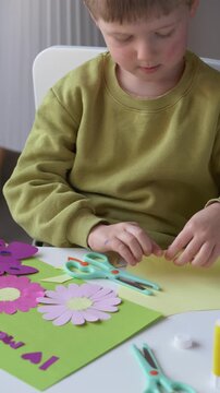 Little boy making mothers day card with paper flowers and glue. Creative activity develops fine motor skills, imagination and artistic abilities in early childhood education. 