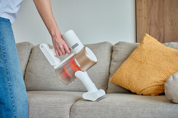 Woman cleaning fabric sofa with handheld vacuum cleaner in living room © barmaleeva