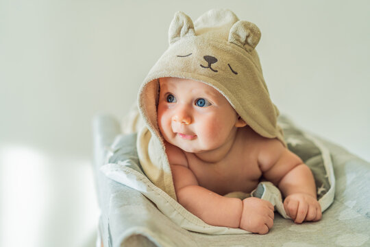 Baby lying on a changing table wrapped in a soft towel after bathing at home. Clean, calm and cozy moment of infant care and safety. Baby hygiene, daily routine and gentle parenting concept