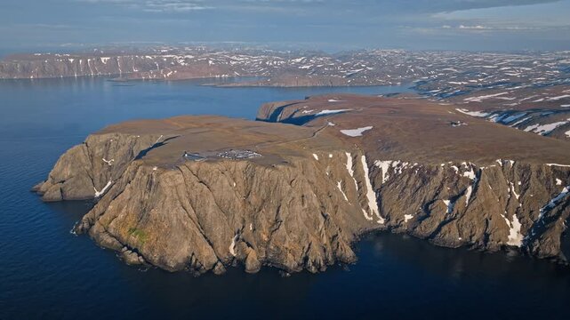 Drone aerial passing the edge of the Nordkapp plateau in Norway. Rugged Arctic cliffs drop steeply into the deep blue Barents Sea.