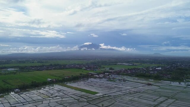 Aerial panoramic view of Kawi and Arjuno mountains peak over lush green rice fields in East Java.