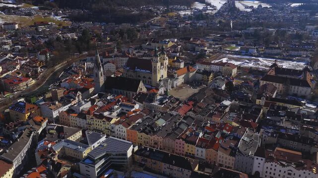 Aerial view shows Brixen Cathedral on the town square, Eisack River curving around the old quarter, pastel buildings with red roofs, and a snowy Alpine valley.