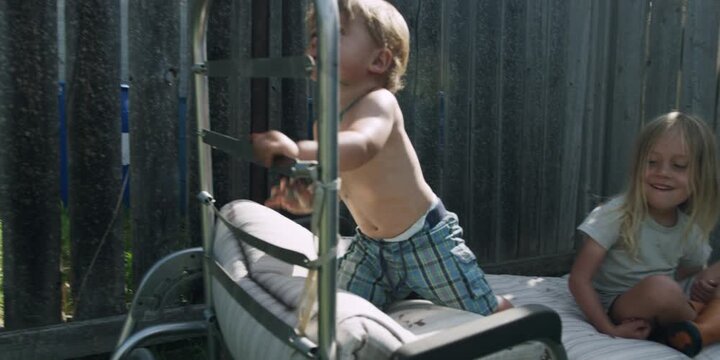 Two children relaxing on a sun lounger outdoors by a wooden fence