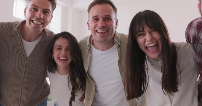 Happy young friends smiling together in a hug. Cheerful group of people laugh at camera at home, sharing unity, support, and friendship in a bright setting. Concept friendship, team, joy, together.