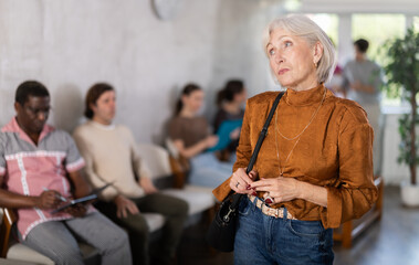 Obraz premium Thoughtful mature woman standing while people waiting in background in reception area