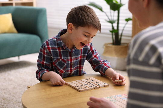 Mother and her happy son playing with educational toys at wooden table indoors, closeup