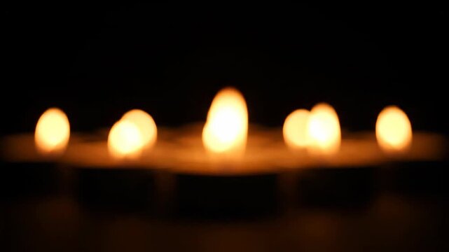 A row of out-of-focus flickering candles creates a warm, abstract bokeh of pulsing amber and gold discs in a dark interior.