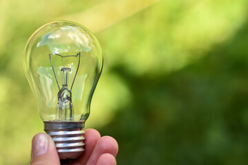 Human hand holding lightbulb on green background. Space for text.Saving earth concept. Renewable, clean, green, energy in nature. Eco-friendly green business,ecology, earth day, csr and net zero. © Katerina Popova
