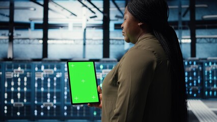 Fototapeta premium Admin with isolated screen tablet in data center implementing advanced power management solutions. Employee using chroma key device to oversee server hub, reducing energy consumption, camera A