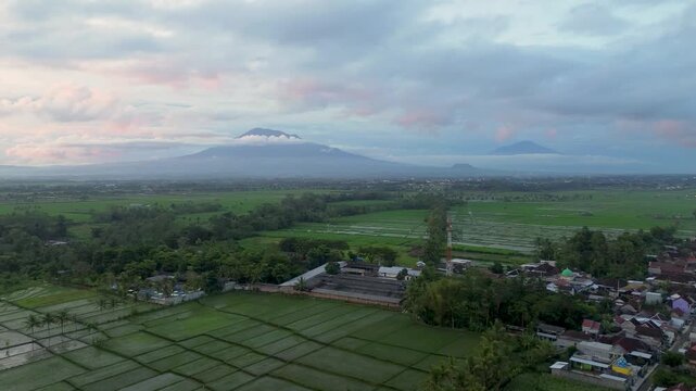 Aerial panoramic view of Kawi and Arjuno mountains peak over lush green rice fields in East Java.