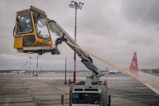 Aircraft de-icing vehicle with elevated platform spraying de-icing fluid on airplane wings at an airport during winter weather conditions