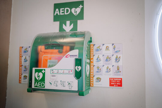 Automated external defibrillator (AED) mounted on wall with first aid instructions and emergency contact information visible nearby