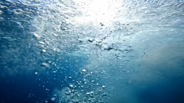 Underwater sunbeams illuminate blue water and seabed sediment stirring in the ocean.