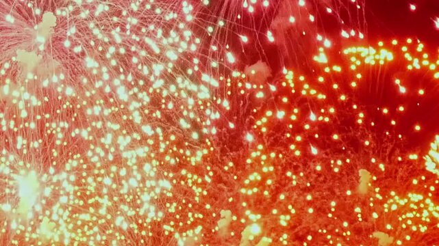 Celebrating Fourth of July, bright bursts of red and gold fireworks ignite the dark evening. Dazzling explosions create a spectacular display of lights over the Summer sky.