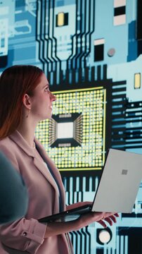 Vertical video Engineering team analyzing semiconductor fabrication with laptop, looking at display. Teamworking PCB factory colleagues oversee microprocessor production with notebook, camera B