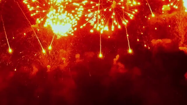 Spectacular, brilliant orange bursts of light erupt in the dark heavens. It's an exciting display of fireworks during an outdoor festival, marking a joyous occasion.
