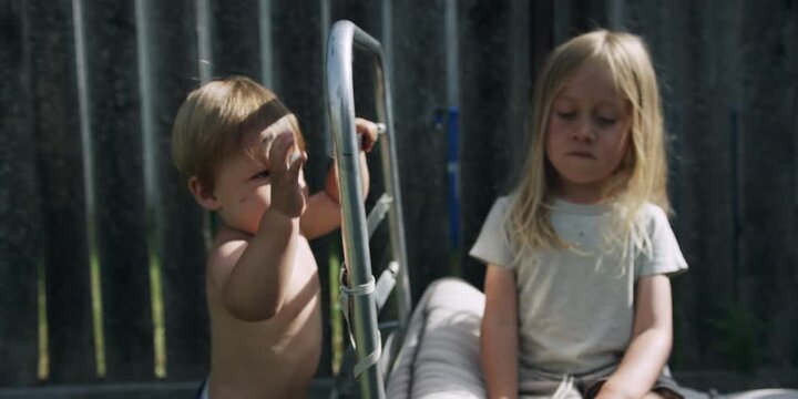 Two young children sitting together in front of a wooden fence