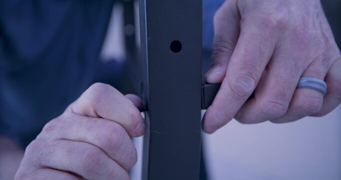 Man screwing screw into metal bar of object - closeup