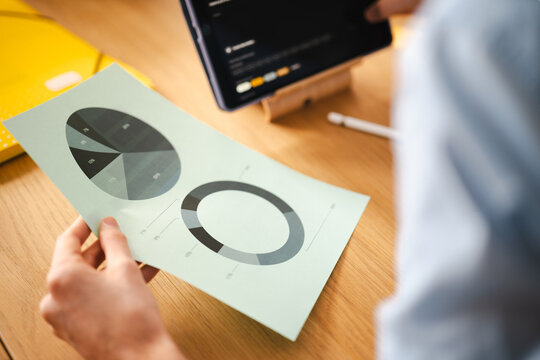 A person reviews financial charts on paper and a tablet, analyzing data for business growth and strategy.