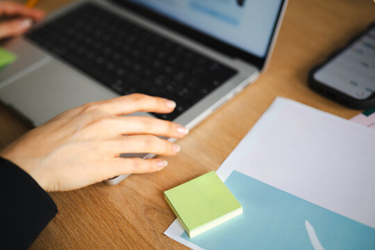 A person's hands are on a laptop keyboard, with a smartphone and a report showing employee job satisfaction statistics on the desk.