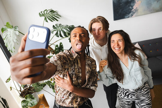 Three friends pose for a selfie, with one sticking out his tongue and the other two laughing joyfully.