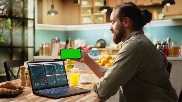 Isolated mockup on mobile phone screen used at home in kitchen, remote worker analyzing metrics and charts on laptop. Teleworking and outsourcing showing task management and research.