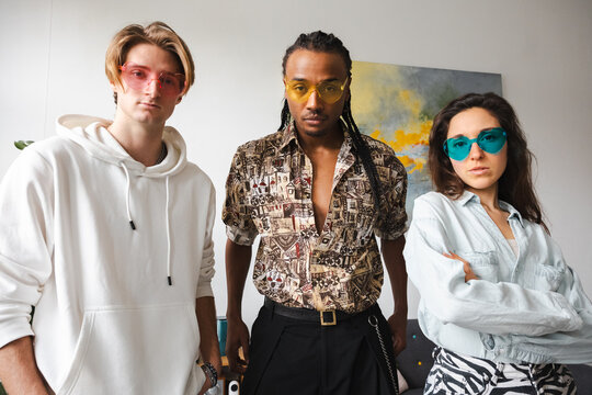Three young adults pose confidently, wearing heart-shaped sunglasses in pink, yellow, and blue, showcasing their unique styles.
