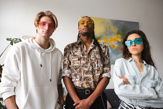 Three young adults pose together, each wearing distinctive heart-shaped sunglasses, conveying a sense of playful individuality and modern style.