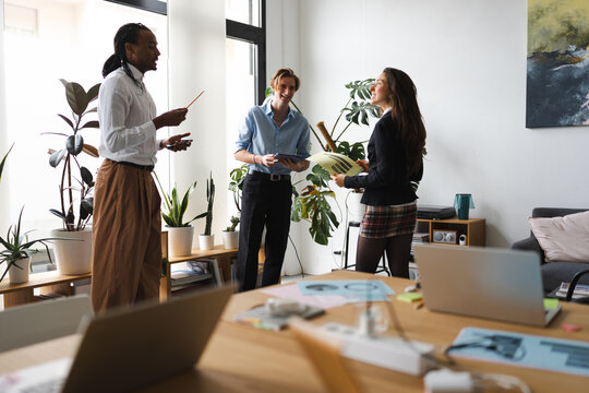 Three colleagues discuss a project in a bright, modern office space, surrounded by plants and laptops.