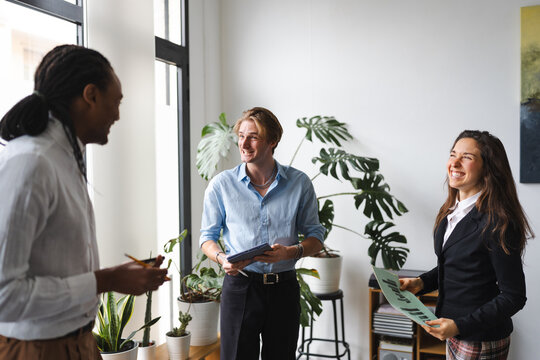Three colleagues in a bright office discuss a document and tablet, sharing ideas and collaborating on a project.