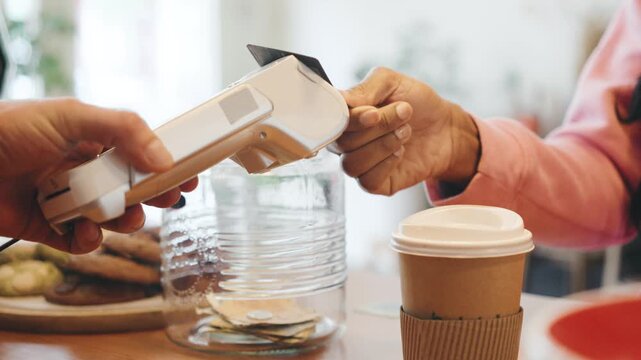 Barista serves customer coffee and processes payment at busy cafe. In a busy cafe during morning rush hour, a customer pays for a drink with a card through a terminal.