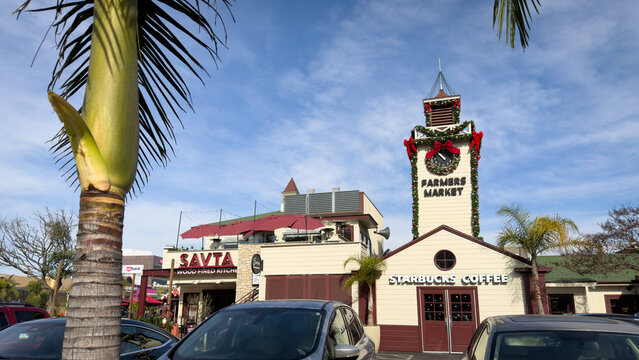 LOS ANGELES, CA, DEC 18, 2025: Farmers Market clock tower and Savta restaurant seen from parking lot, decorated for winter holidays,  palm trees framing