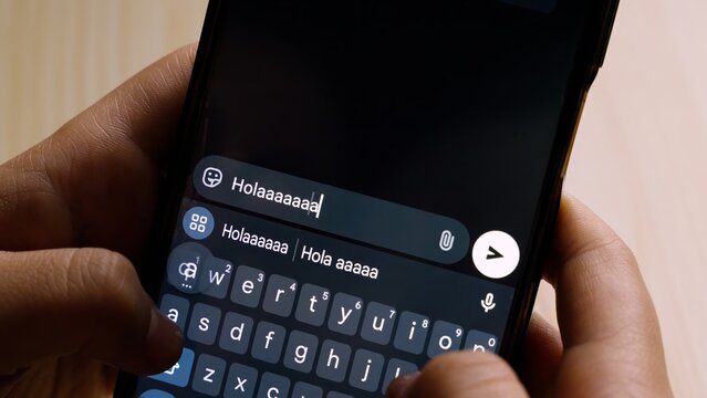 Close-up of hands holding a smartphone while typing "Hola!" (Hello!) in a messaging app.