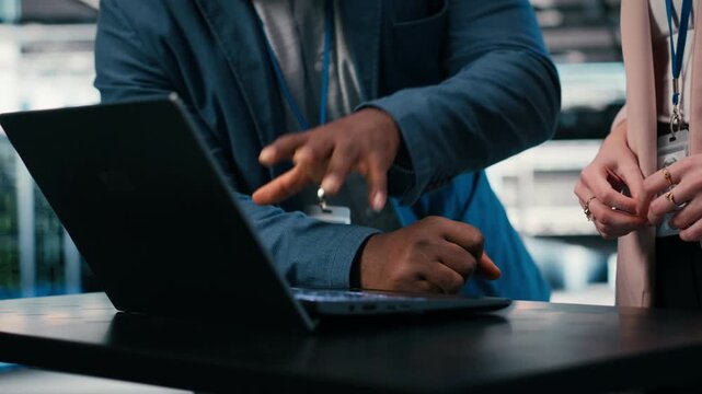 Monitoring power consumption, laptop and engineering team in server hub cooperating. Overseeing hardware, brainstorming and coworkers in data center ensuring industry standards compliance, camera B