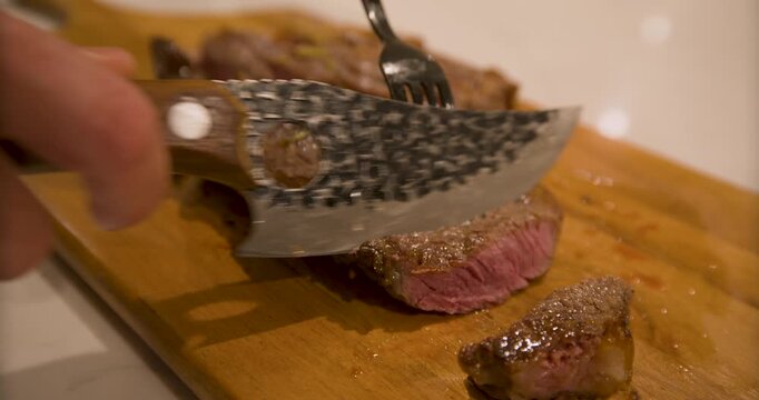 Closeup on sharp knife cutting rare stake on wood board - handheld shot