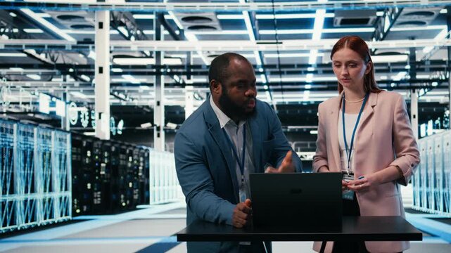 Server hub engineering team using laptop to monitor power consumption, cooperating. Data center coworkers brainstorming, overseeing hardware, ensuring industry standards compliance, camera A