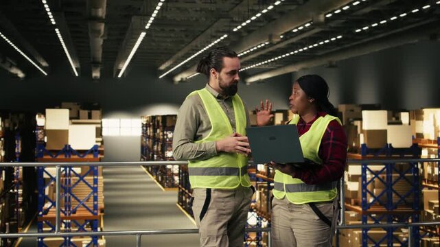 Multicultural team collaborating in industrial warehouse on platform, two workers coordinate parcel handling and shipping workflow. Supply chain control to ensure e-commerce operations.