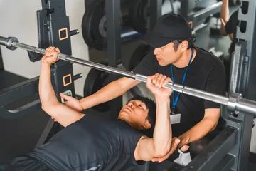 Fotobehang Sportschool A young Asian man receiving personal training at a gym.  © buritora