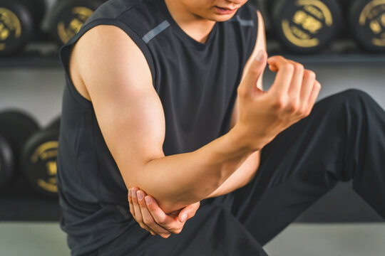 A young Asian man complains of elbow pain while training at the gym.