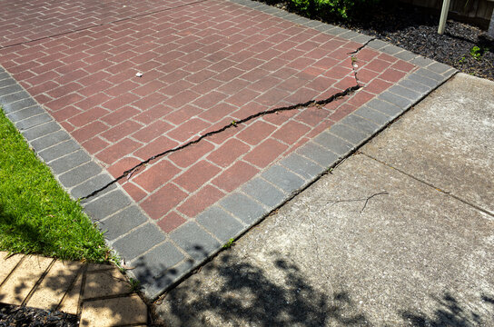 Cracked brick driveway in a residential property, showing surface damage and structural wear. A common suburban maintenance issue highlighting ground movement, aging materials, and property upkeep