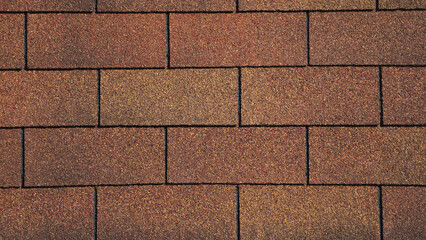 A close-up of brown and tan asphalt roof shingles arranged in a staggered rectangular pattern. The surface features a gritty, granular texture with subtle variations in earth-toned shades. © Everlasting Dreams