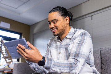 Fototapeta premium Adult man holding tablet in folio case and smiling while sitting on couch at home office