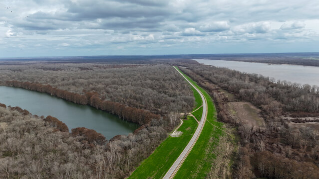 Aerial view showing la 15 highway running on top of the mississippi river levee, separating the river from a backwater lake and vast bare cypress swamp forests in vidalia, louisiana