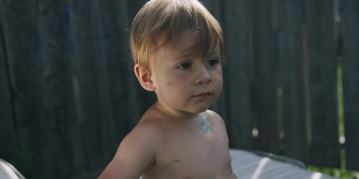 Toddler standing by a wooden fence on a sunny day
