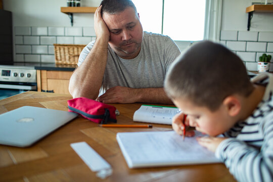 Tired father helping son with homework at home kitchen table