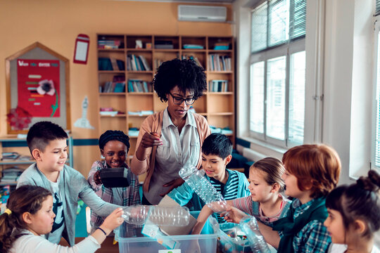 Teacher and elementary students recycling plastic in classroom