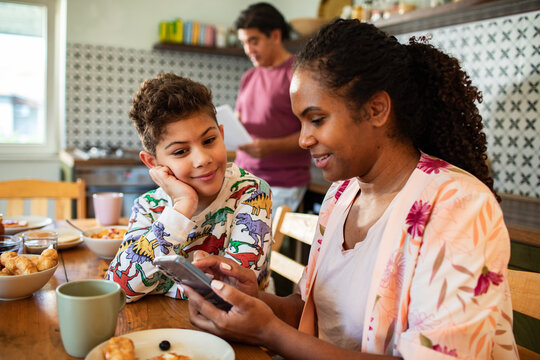 Mother and son using smartphone at breakfast in home kitchen